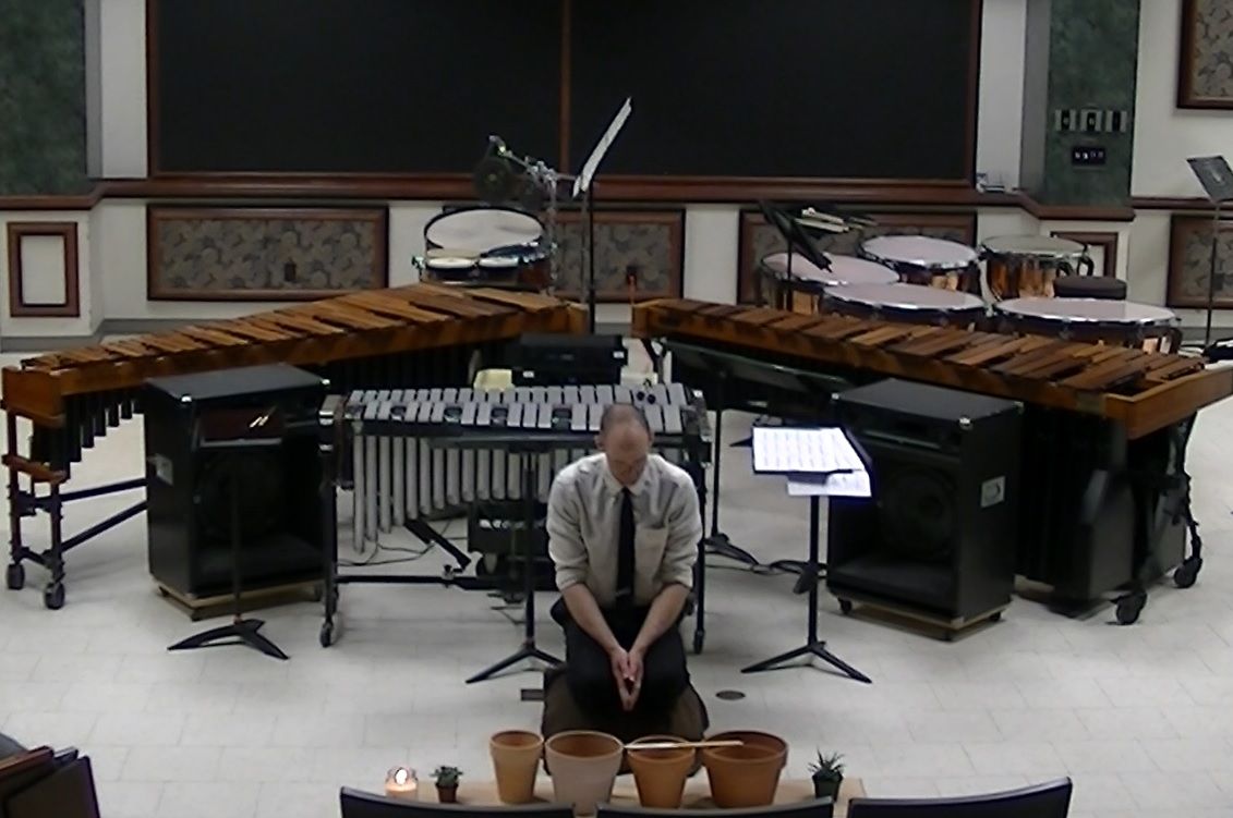 Dr. Shuey seated behind four flowerpots for Frederic Rzewski’s To the Earth